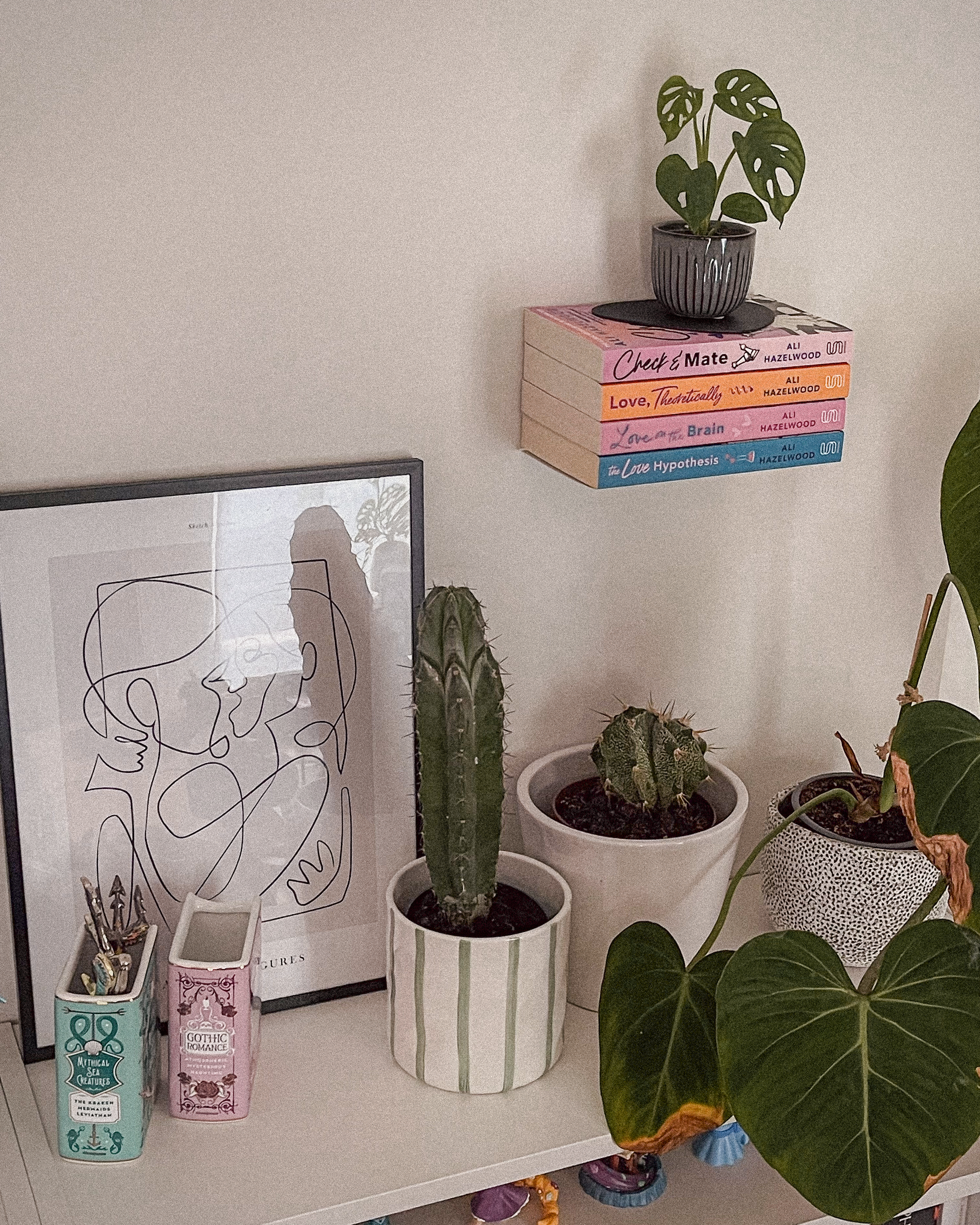 Plants, art and ceramic books on bookshelves, floating books on the wall